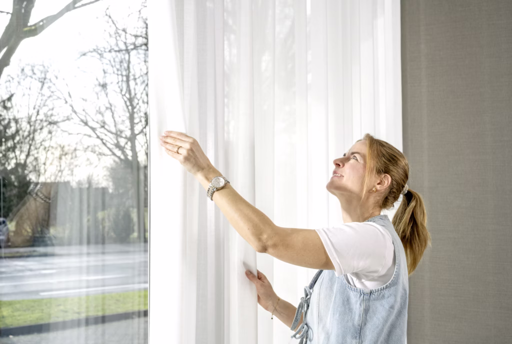 Dekorateurin richtet einen leichten Vorhang am Fenster